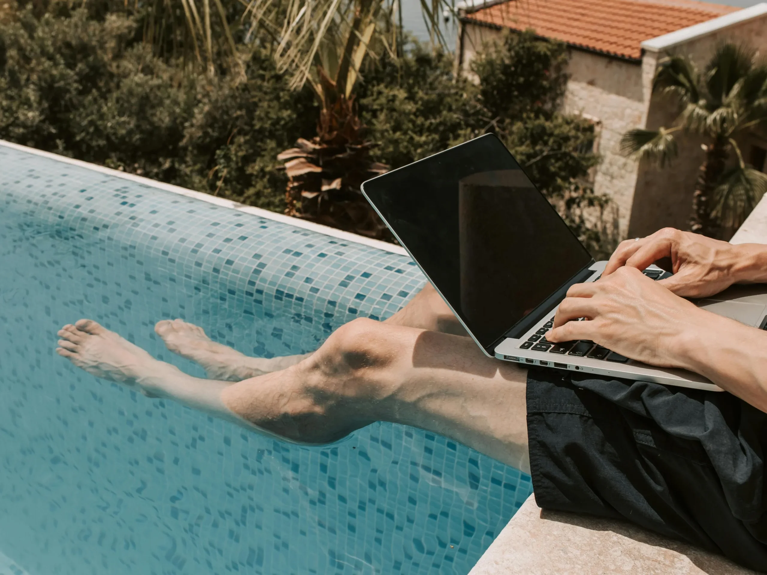 Person working on a laptop by a plaster swimming pool, illustrating pool maintenance.