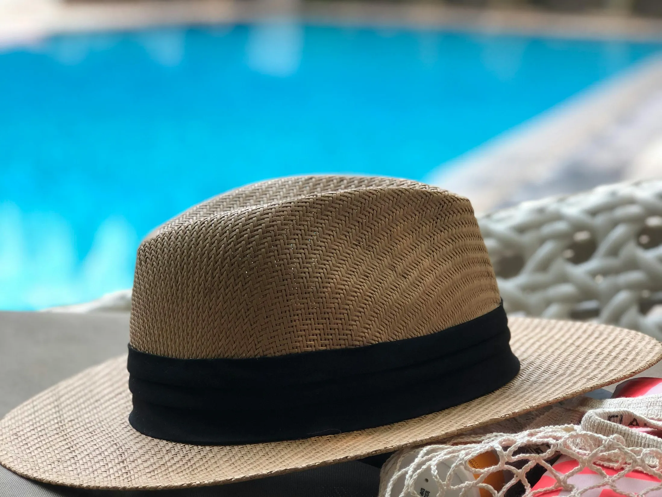 A straw hat placed near a swimming pool, representing relaxation after adding baking soda or soda ash.